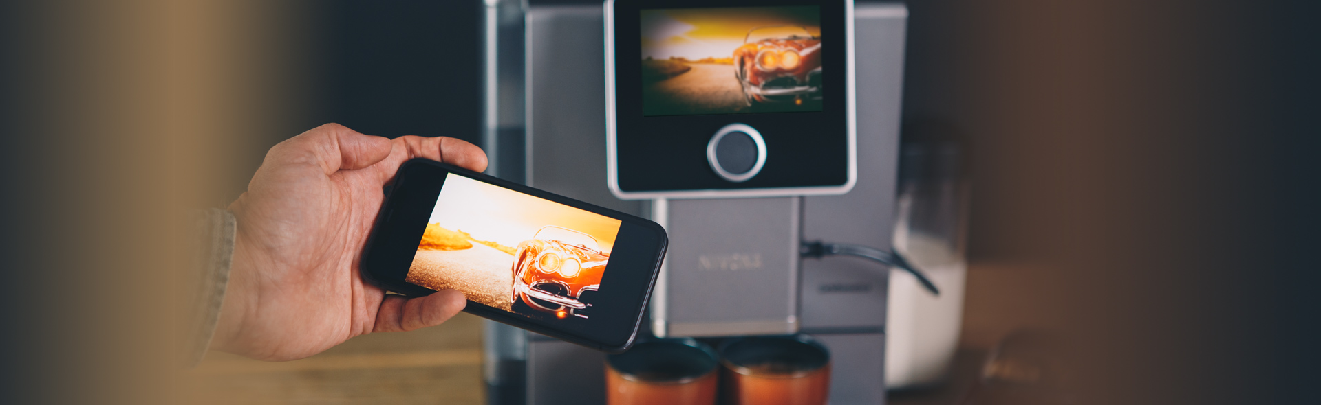 Handy zeigt gleiches Bild wie das Display der Kaffeemaschine im Hintergrund