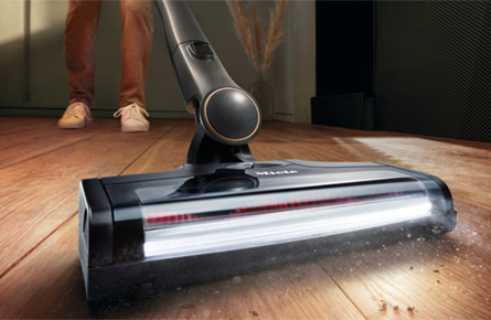 Staubsauger saugt auf dunklem Holsboden.